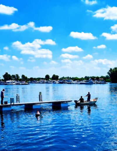 Menschen angeln auf einem Steg und in einem Boot auf einem ruhigen See unter blauem Himmel mit weißen Wolken