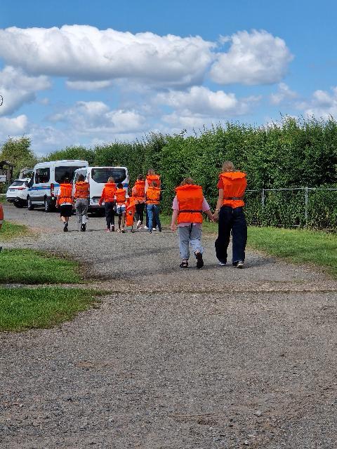 Gruppe von Menschen, darunter Kinder und Erwachsene, gehen auf einem Weg und tragen orangefarbene Sicherheitswesten